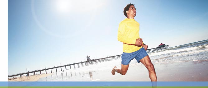 A man with blue pants and yellow shirt jogging on the beach